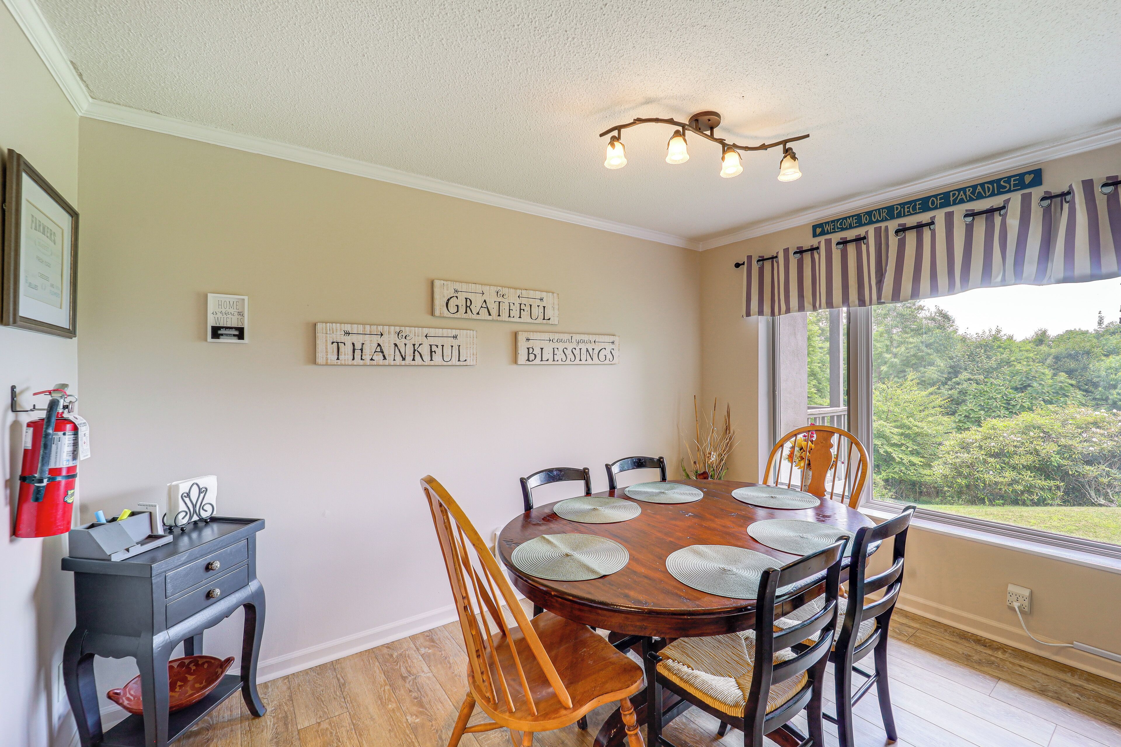 A dining area with a wooden table, chairs, and placemats. There are wall decorations with inspirational phrases and a fire extinguisher on the wall.