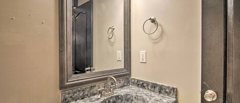 Un baño con lavamanos de granito, un espejo grande y un aro para toallas en la pared.