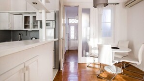 A modern kitchen with white cabinetry and a dining area with a white table and chairs. - Basilica View Apartment With Balcony (Budapest)
