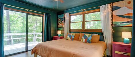 A bedroom with a large bed, a ceiling fan, and a view of the outdoors.