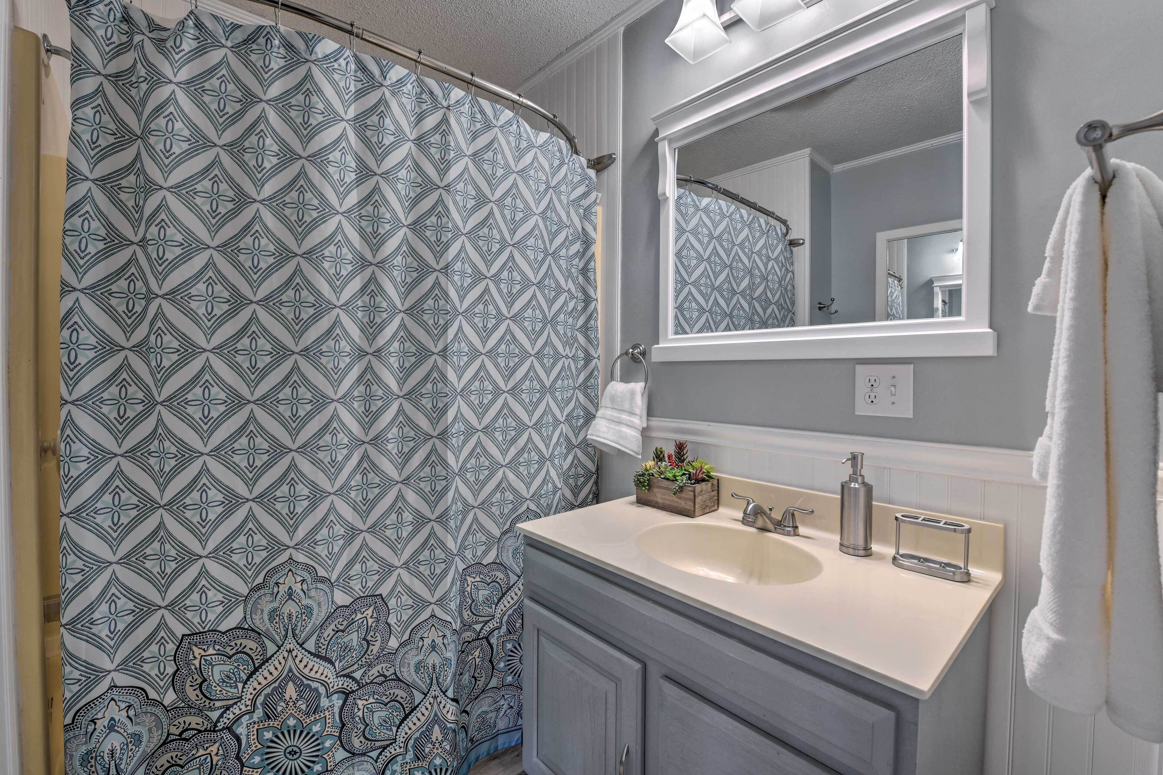 A bathroom with a patterned shower curtain, a sink with a mirror above it, and a towel hanging on the wall.