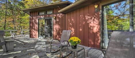 Une terrasse en bois avec des sièges d’extérieur et une porte vitrée donnant sur un espace abrité.