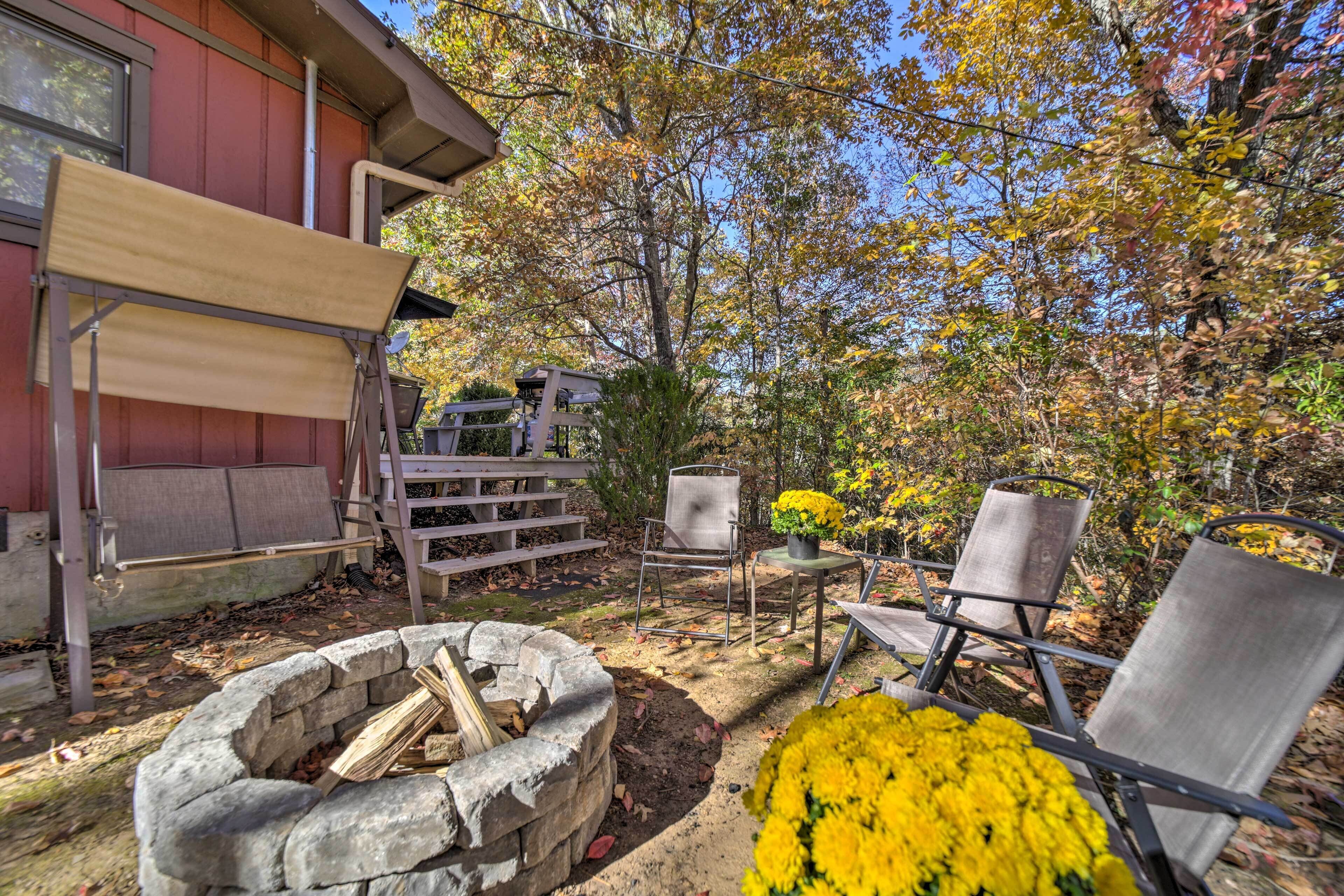 A patio area with a fire pit, outdoor seating, and a view of trees.