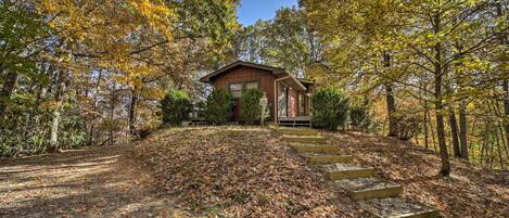 A cabin with a wooden exterior, surrounded by autumn foliage and a stone staircase leading to the entrance.