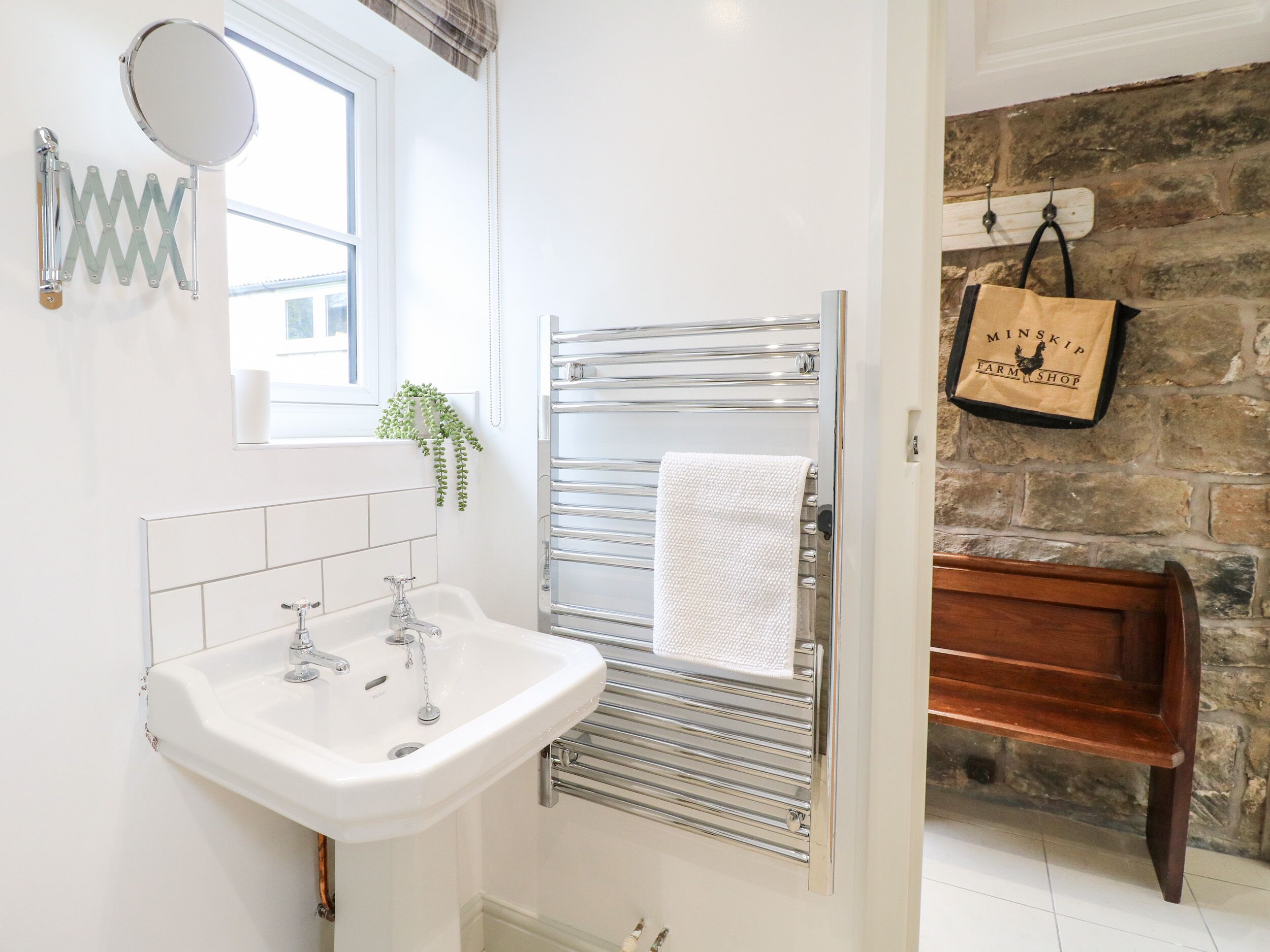 Une salle de bain avec un lavabo blanc, un miroir, un porte-serviettes et un mur en pierre.