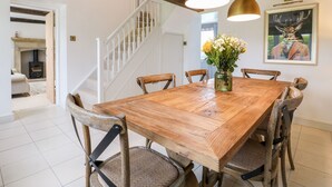 A wooden dining table with six chairs, a vase with flowers, and a staircase in the background. - Sycamore Cottage (Ashbourne)