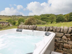 Un jacuzzi con un fondo de pared de piedra, rodeado por un paisaje rural con campos y árboles.