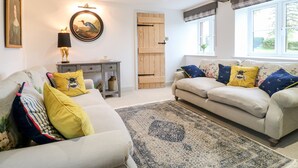 A living room with a sofa set, a coffee table, a rug, a lamp, a painting, and a wooden door. - Sycamore Cottage (Ashbourne)