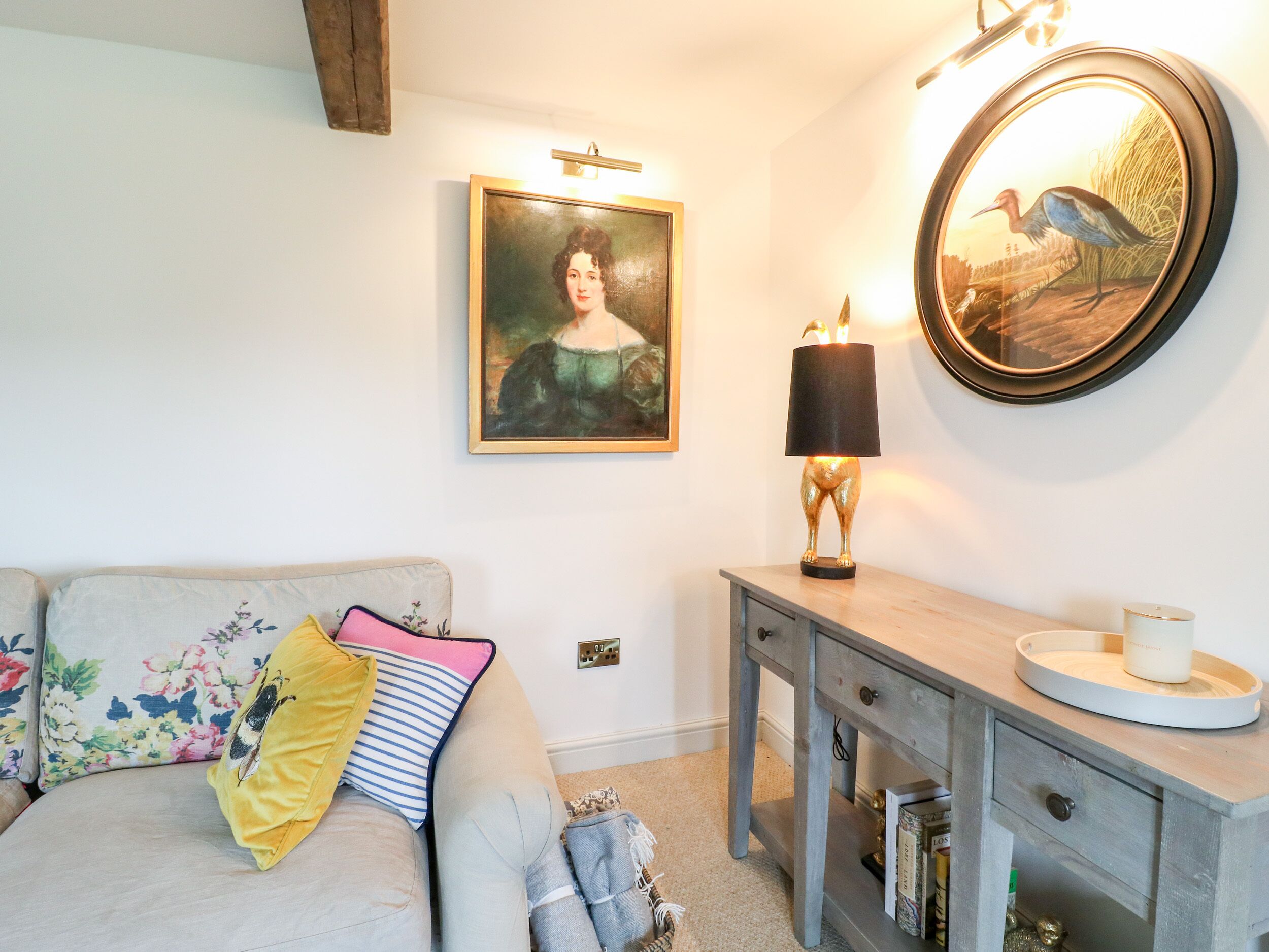 A living room with a sofa, a side table, a lamp, a framed painting, and a round mirror.