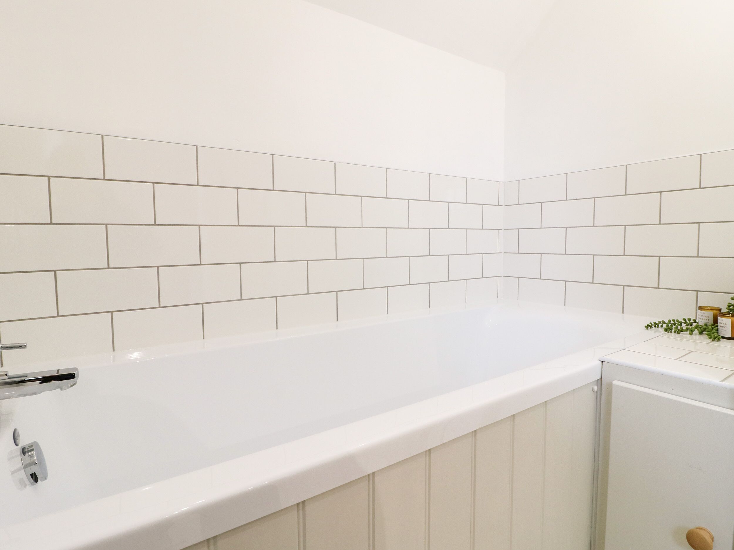 A white bathtub with a chrome faucet in a bathroom with white tiled walls.