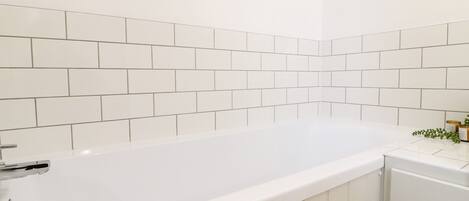 A white bathtub with a chrome faucet in a bathroom with white tiled walls.