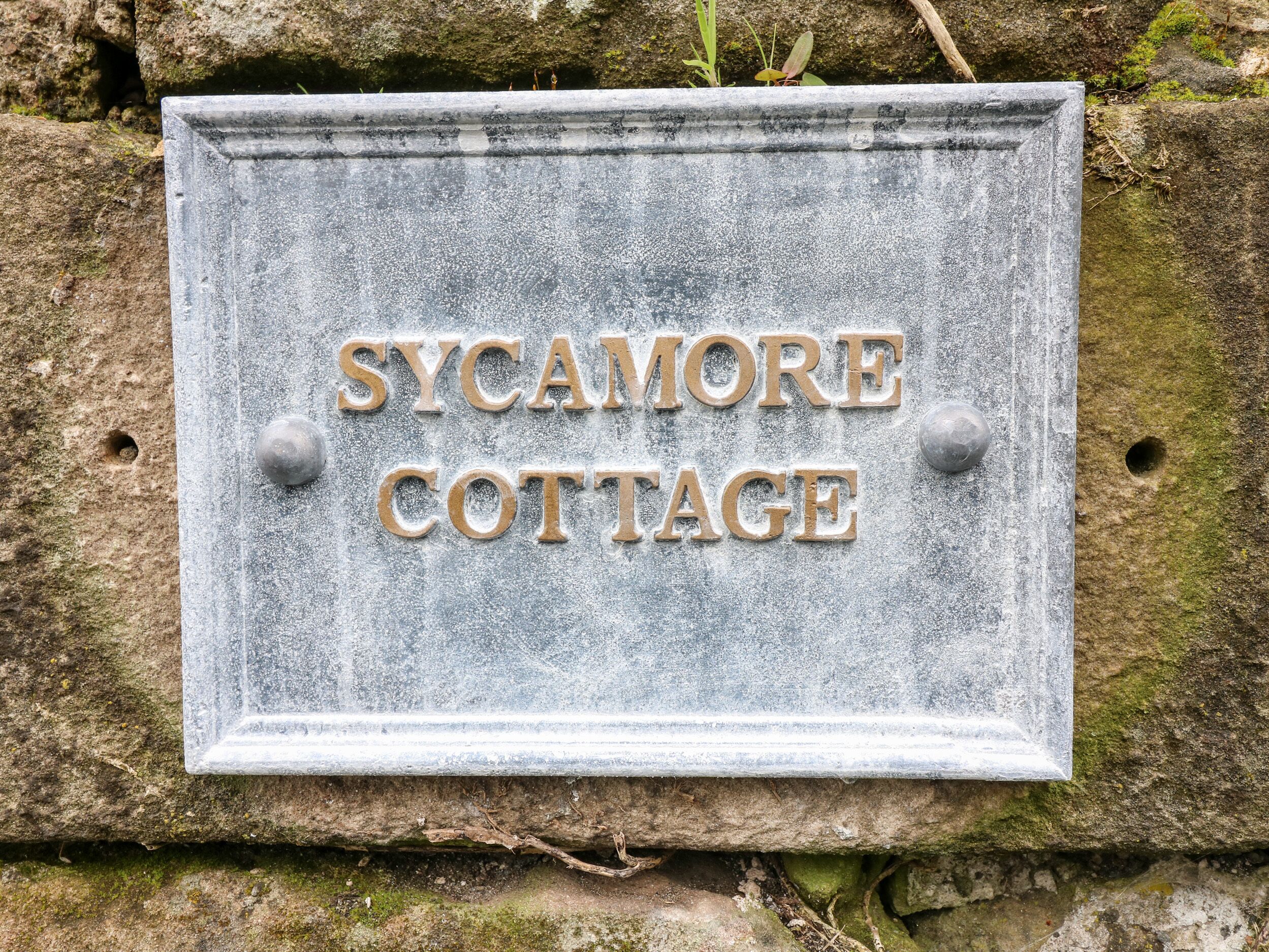 Una señal de piedra con la inscripción 'SYCAMORE COTTAGE'.