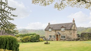 A stone house with a well-maintained lawn, a stone wall, and a garden with various plants. - Sycamore Cottage (Ashbourne)