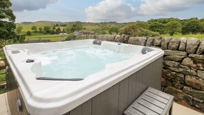 A hot tub on a deck with a stone wall backdrop, overlooking a rural landscape. - Sycamore Cottage (Ashbourne)