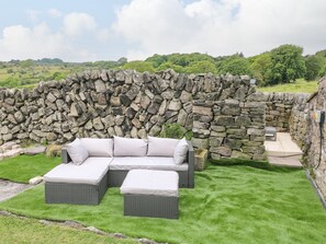Un muro de piedra con un sofá y un reposapiés de mimbre en una zona cubierta de césped.