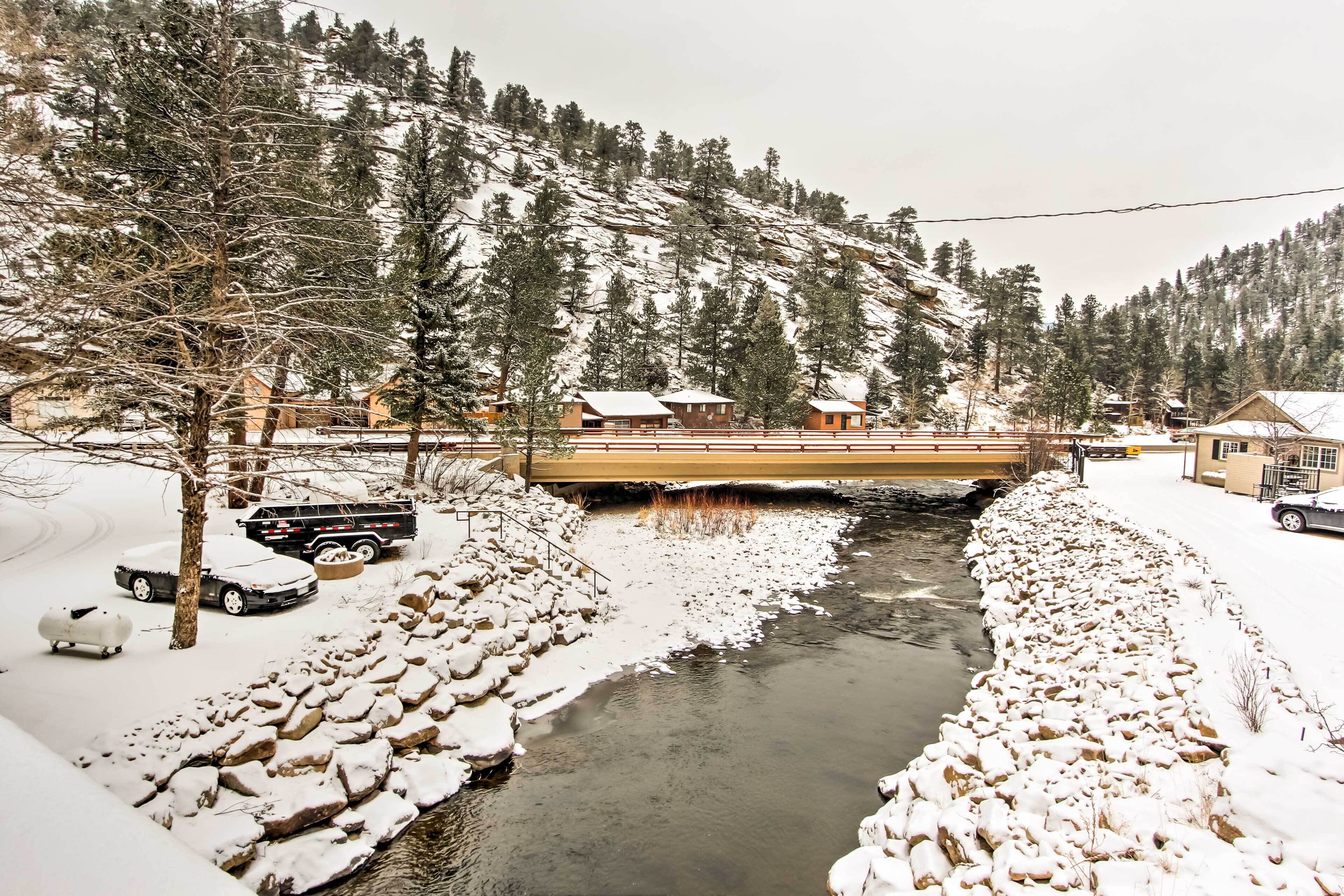 Schneebedeckte Landschaft mit Fluss, Holzhäusern und einer Brücke.