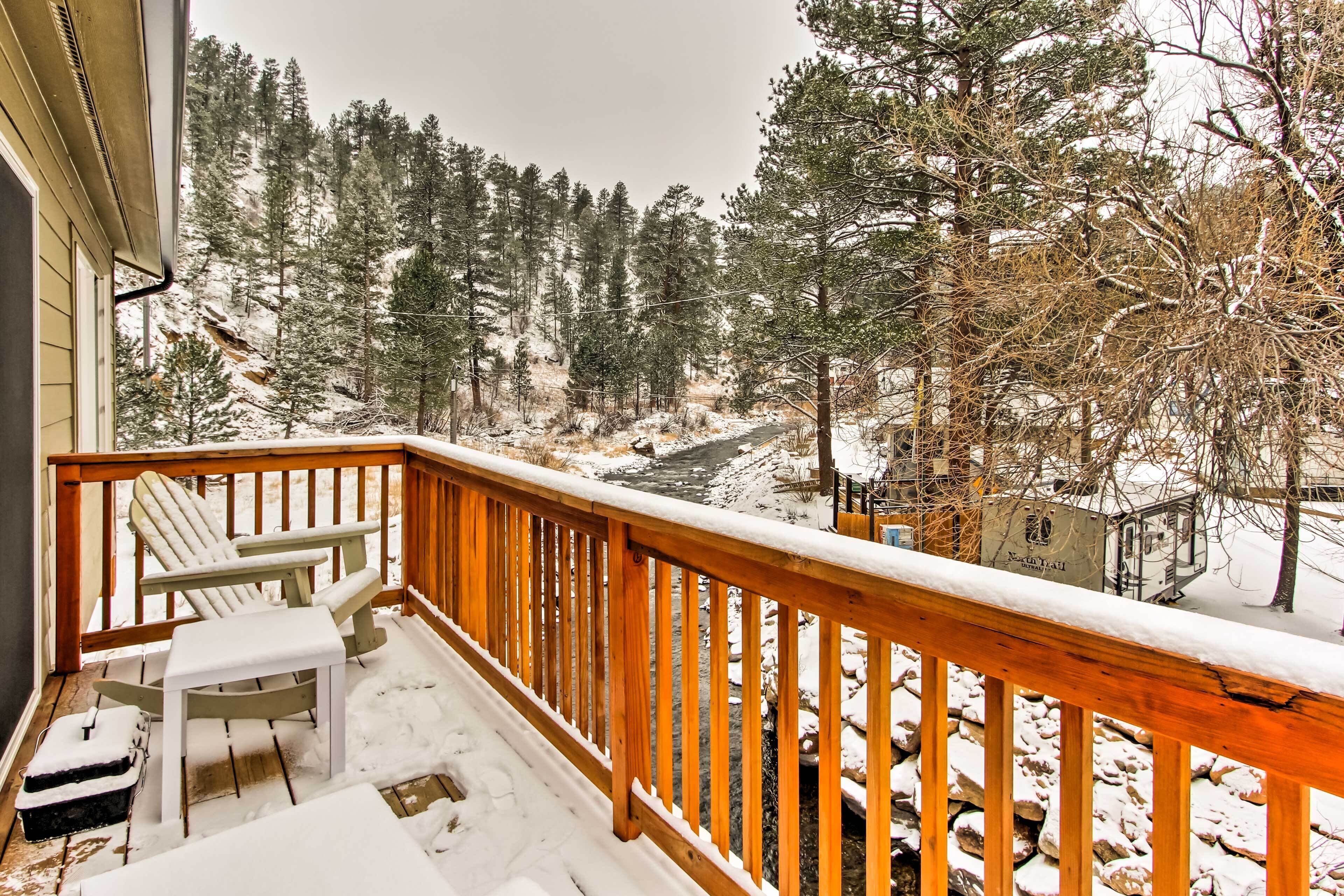 A wooden deck with a snow-covered railing, a chair, and a table.