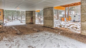 A spacious interior with exposed concrete pillars, a dirt floor, and large windows offering a view of a snowy forest and a North Trail RV. - Drake Home on Big Thompson River - 3 Mi. to Estes! (Drake)