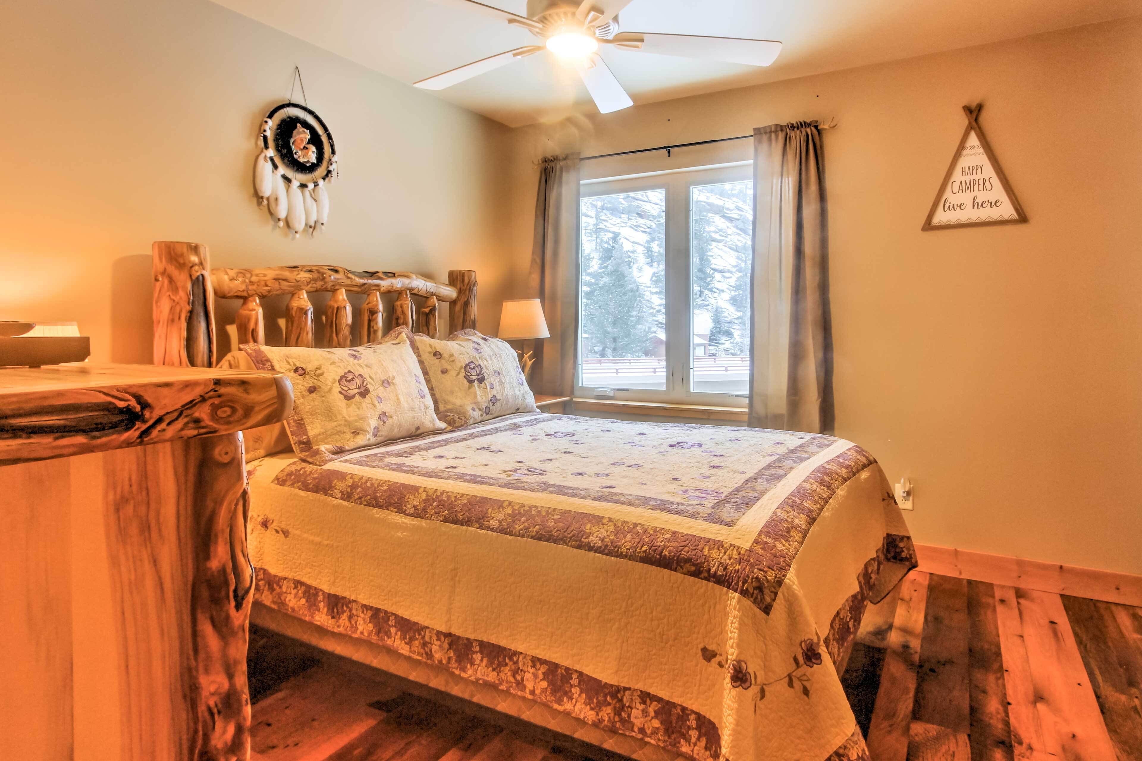 Una camera accogliente con un letto dal telaio in legno rustico, una ventola a soffitto, un portafortuna e un cartello con su scritto 'Happy Campers Live Here'.