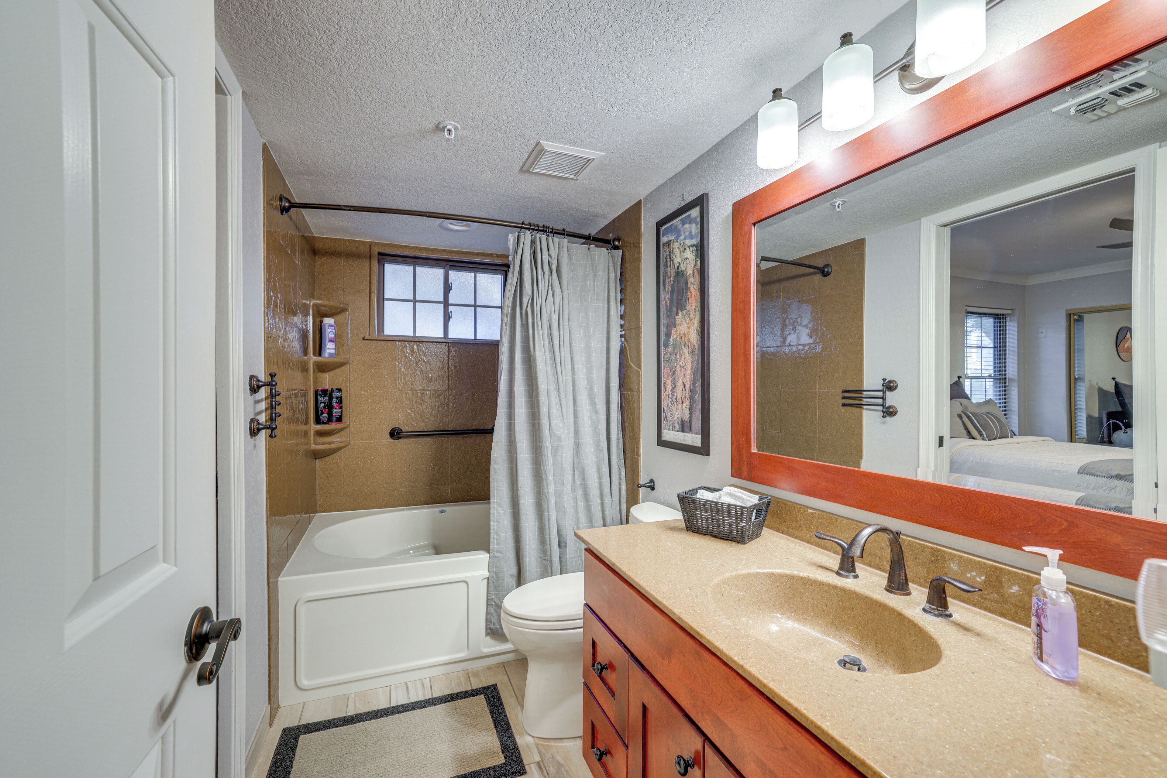 A bathroom with a bathtub, toilet, vanity with a sink, and a large mirror.