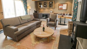 A cozy living room with a sofa, armchair, and a round coffee table. There's a kitchen area in the background with cabinets and a stove. - Bolton Cottage (Appleby-in-Westmorland)