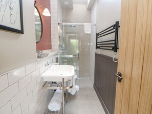 A modern bathroom with a white sink, glass shower enclosure, and a wooden door. - Bolton Cottage (Appleby-in-Westmorland)