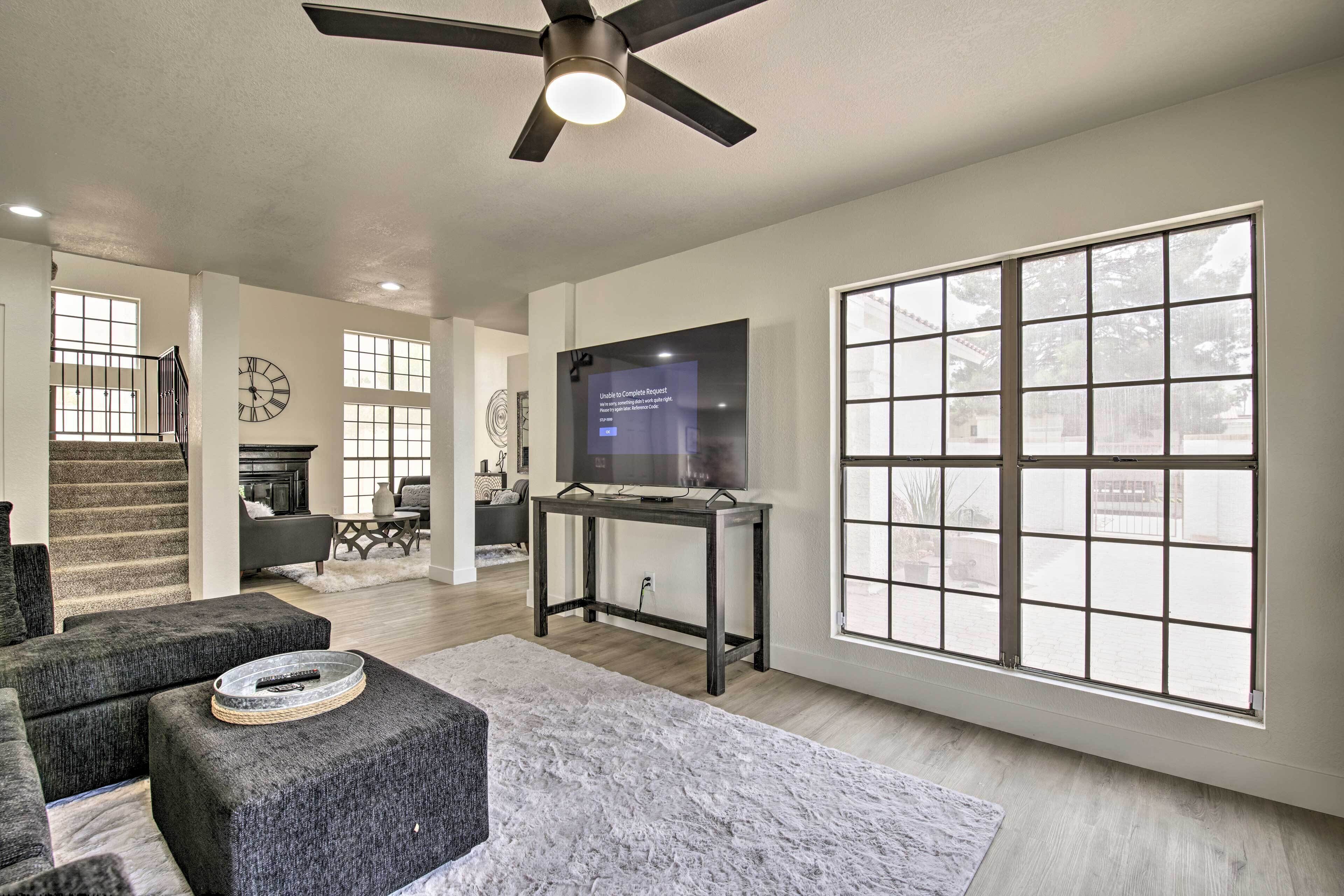 A spacious living room with a large window, a ceiling fan, and a flat-screen TV on a stand.