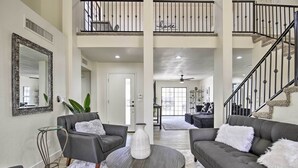 A spacious living room with a grey sofa, a round coffee table, and a large mirror. A staircase with a 'home' sign is visible in the background. - Hot Tub! Family-friendly Home, 8 Mi to Westgate (Glendale)