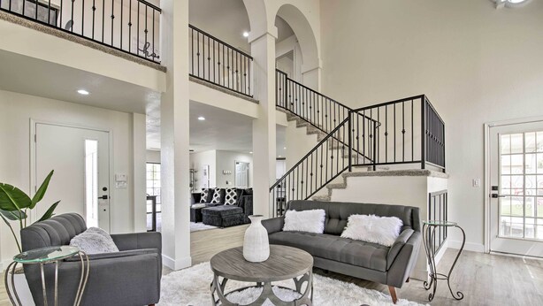 A spacious living room with a grey sofa, a round coffee table, and a staircase with a black railing. - Hot Tub! Family-friendly Home, 8 Mi to Westgate (Glendale)