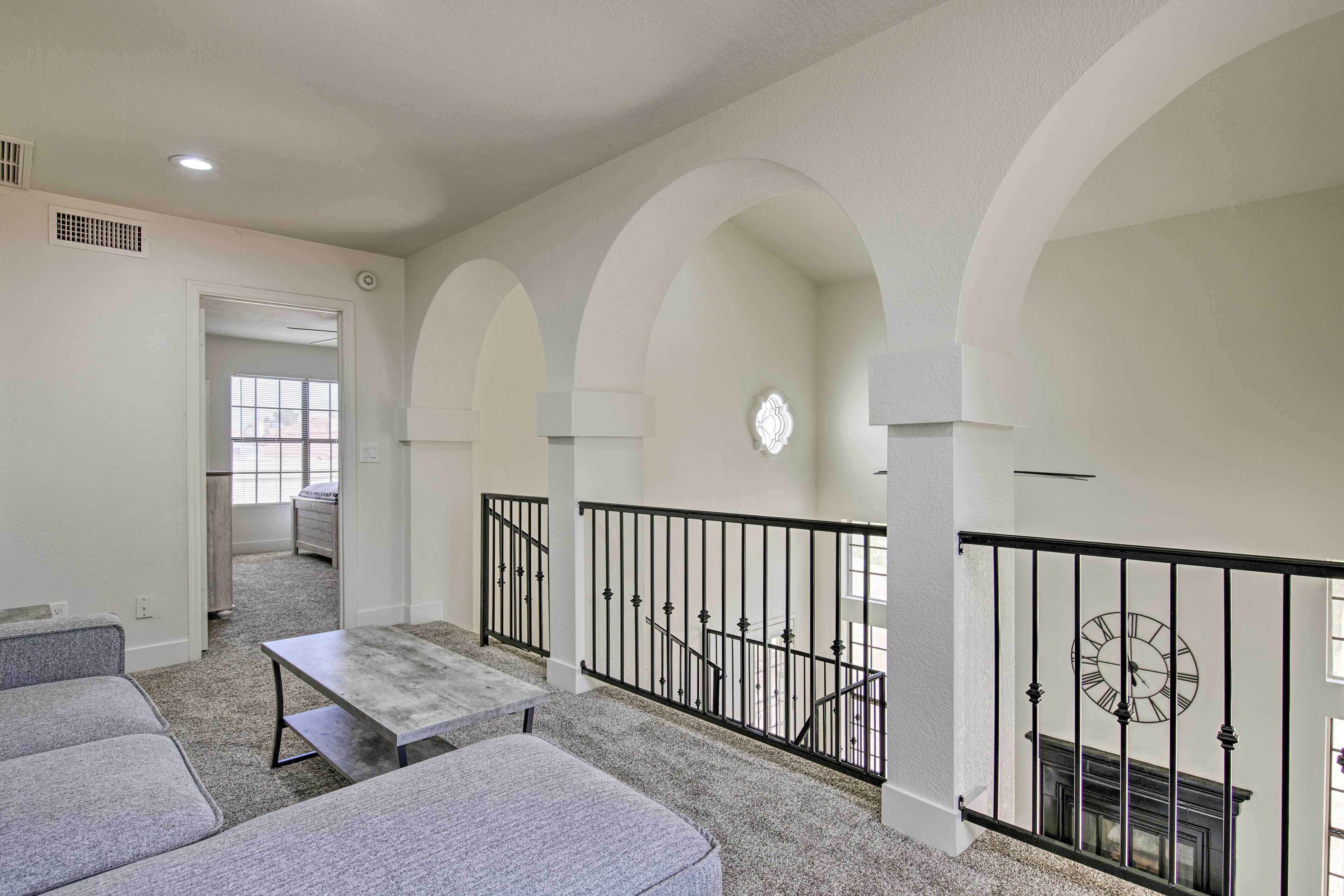 A spacious living area with a high ceiling, a staircase with a black railing, and a fireplace.