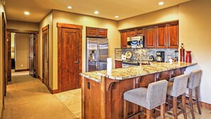 A kitchen with wooden cabinets, stainless steel appliances, a granite countertop, and a bar area with stools. - Ski-in/ski-out Breckenridge Resort Condo at Peak 7 (Breckenridge)