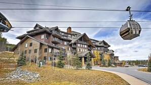 A multi-story building with a ski lift cable car in the foreground. - Ski-in/ski-out Breckenridge Resort Condo at Peak 7 (Breckenridge)