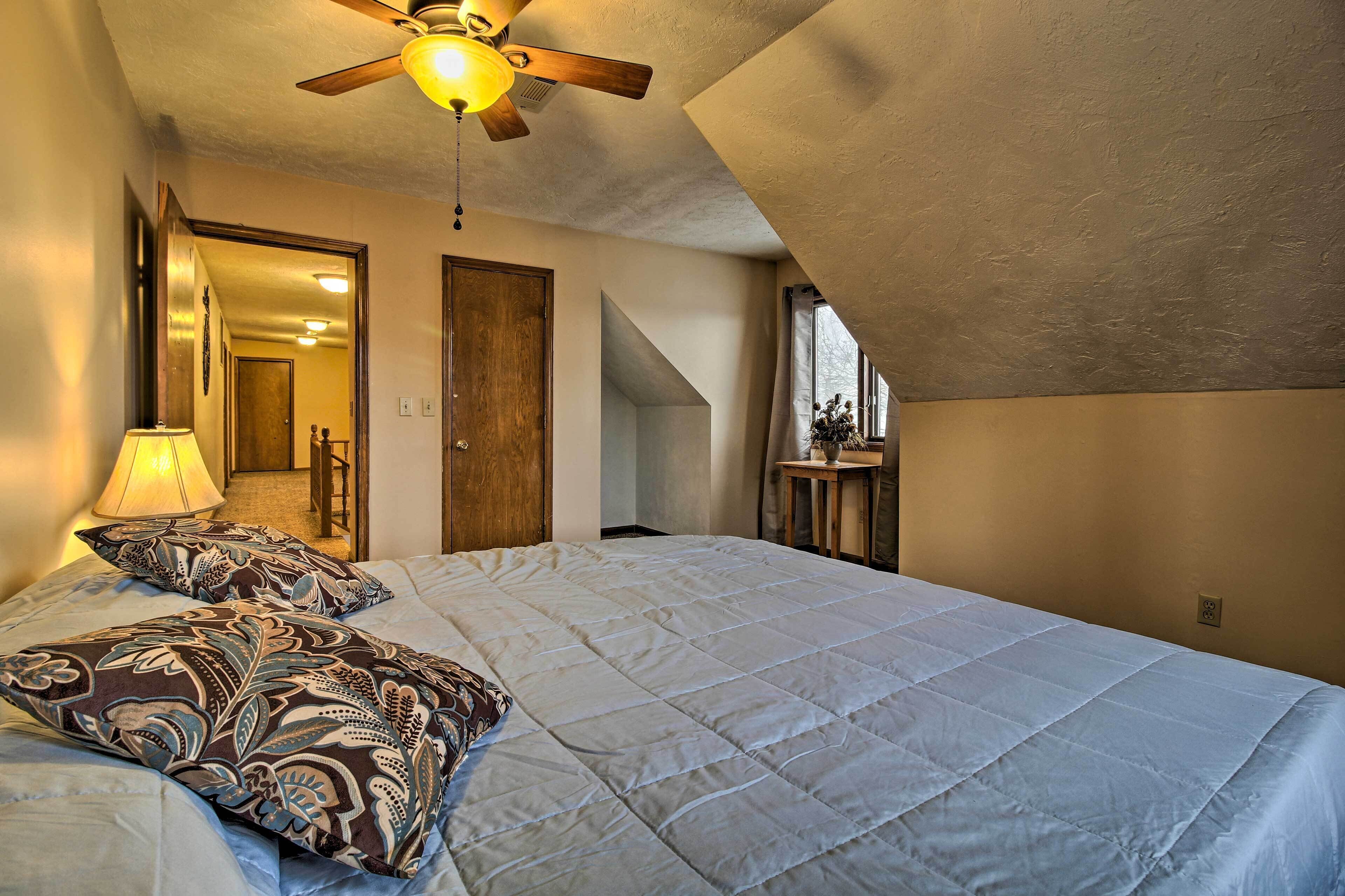 A bedroom with a bed, a ceiling fan, a lamp, and a window.