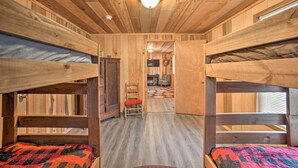 A cabin with bunk beds, wooden walls, a ceiling light, and a hallway leading to a living area. - Remote Kentucky Cabin w/ Fire Pit & 2 Ponds (New Concord)