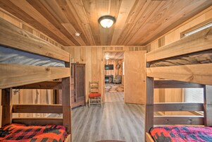 Una cabaña con literas, paredes de madera, una lámpara en el techo y un pasillo que conduce a una sala de estar.