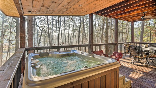A wooden deck with a hot tub, outdoor furniture, and a view of trees.
