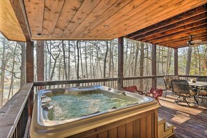 Eine Holzterrasse mit Whirlpool, Gartenmöbeln und Blick auf Bäume.