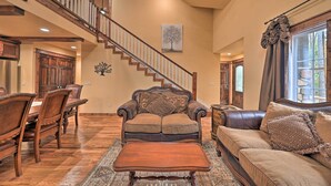 A spacious living room with a wooden staircase, a dining area with a large wooden table and chairs, and a cozy seating area with a sofa and armchair.