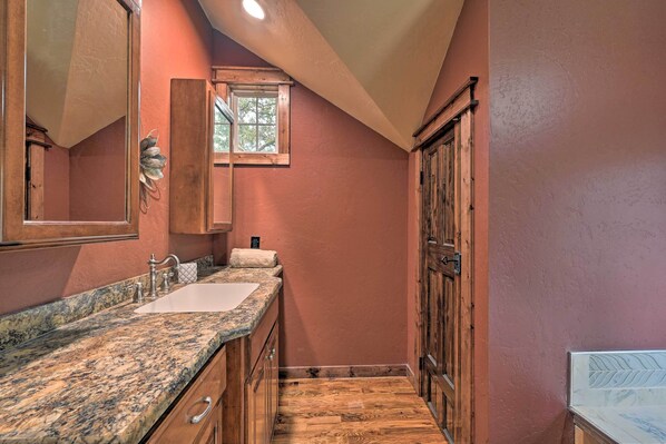 A bathroom with a wooden vanity, a sink, and a mirror. - Tudor-style Broken Bow Cottage w/ Hot Tub & Decks! (Broken Bow)