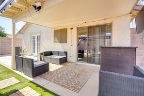 Une terrasse couverte, meublée de meubles en osier, avec une porte-fenêtre coulissante et un tapis à motifs.