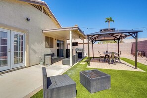 Une terrasse avec mobilier d’extérieur, un espace barbecue couvert et une pelouse bien entretenue.
