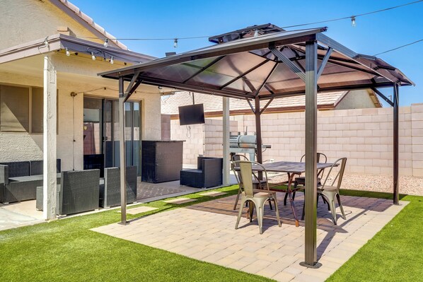 Un espace extérieur aménagé en terrasse, avec un coin salon couvert, un barbecue et un téléviseur fixé au mur.