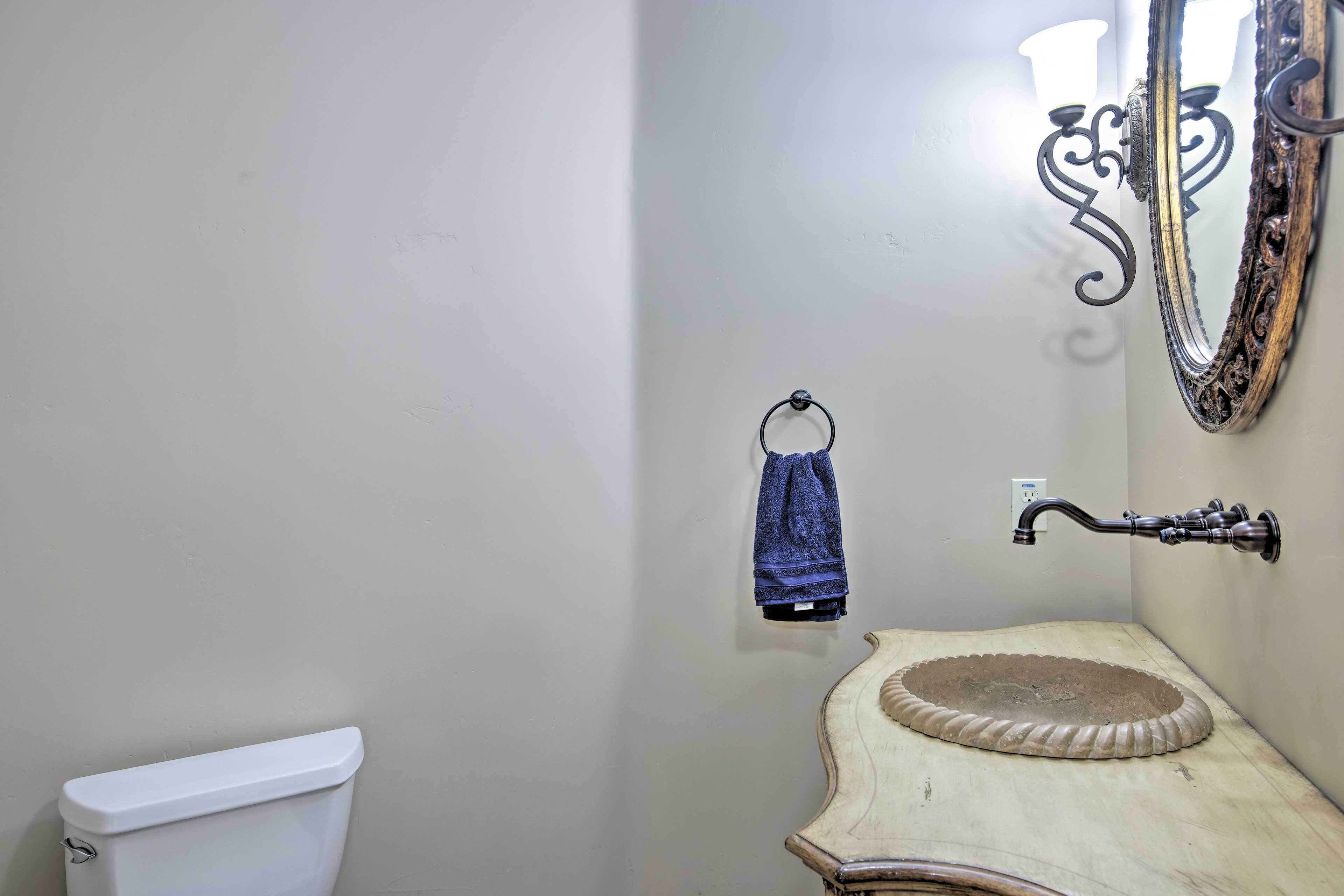 A bathroom with a white toilet, a vintage sink with a decorative basin, a towel ring with a blue towel, and a wall-mounted mirror with an ornate frame.