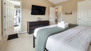 Une chambre à coucher comprenant un lit, une commode, un téléviseur et une porte donnant sur une autre pièce.
