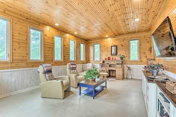 A cozy cabin interior with wooden walls, a dining area, and a seating area with a coffee table and chairs. - Charles Town Home w/ Private Pool & Hot Tub (Charles Town)