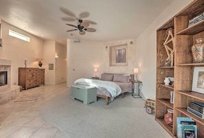 Ein Schlafzimmer mit einem Bett, Nachttischen, einem Bücherregal, einem Kamin und einem Deckenventilator.