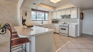 A modern kitchen with white cabinetry, a central island, and a dining area with metal chairs.
