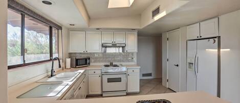 A modern kitchen with white cabinets, a stainless steel refrigerator, a microwave, and a large window providing natural light.
