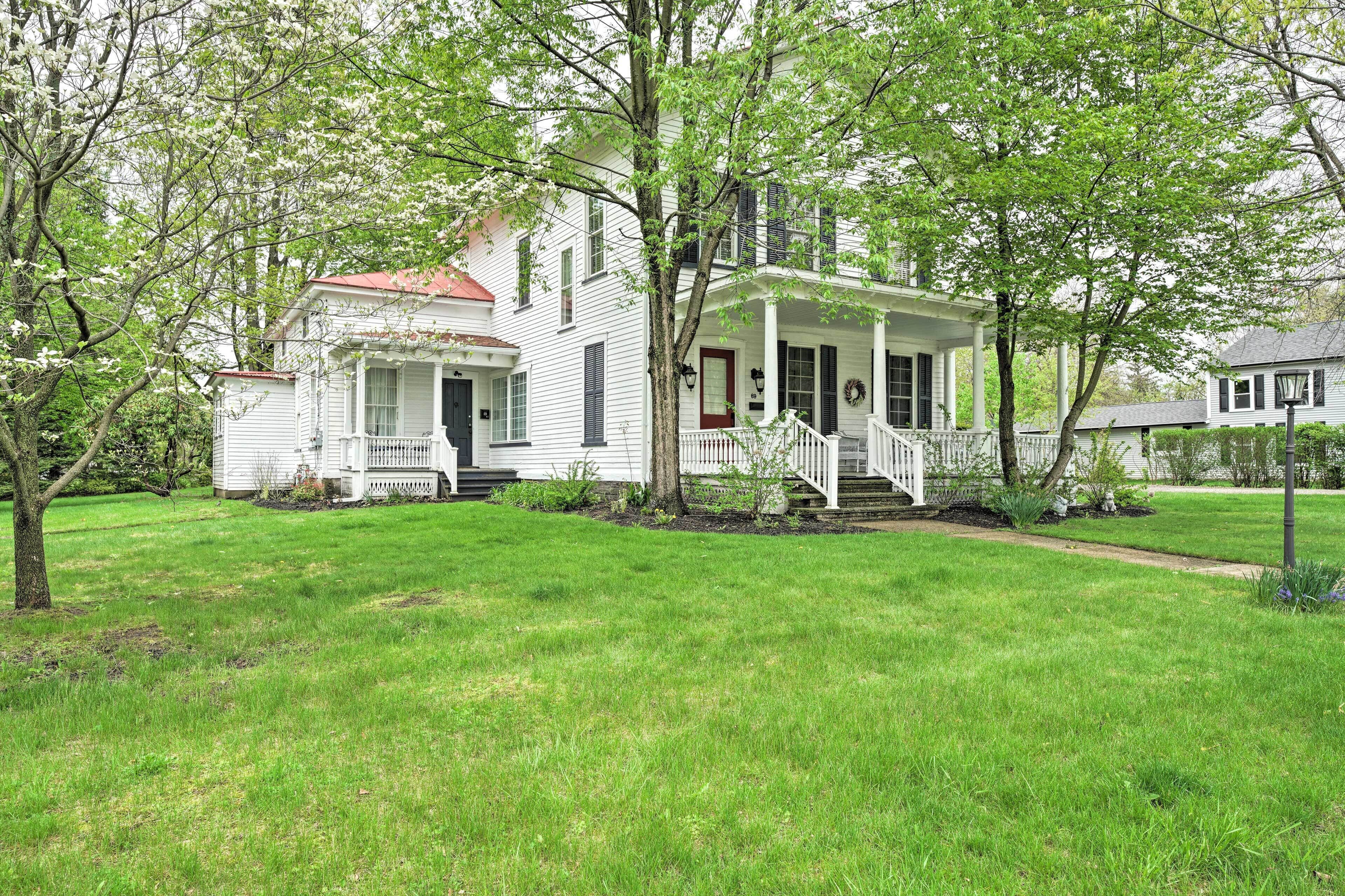 A white two-story house with a porch and a red roof.