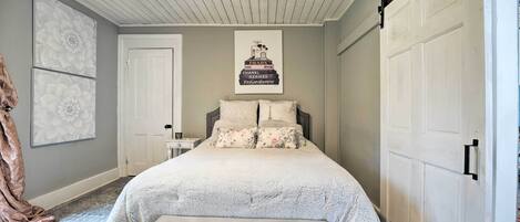 A bedroom with a bed, a bedside table, a nightstand, a ceiling fan, a door, and a poster on the wall.